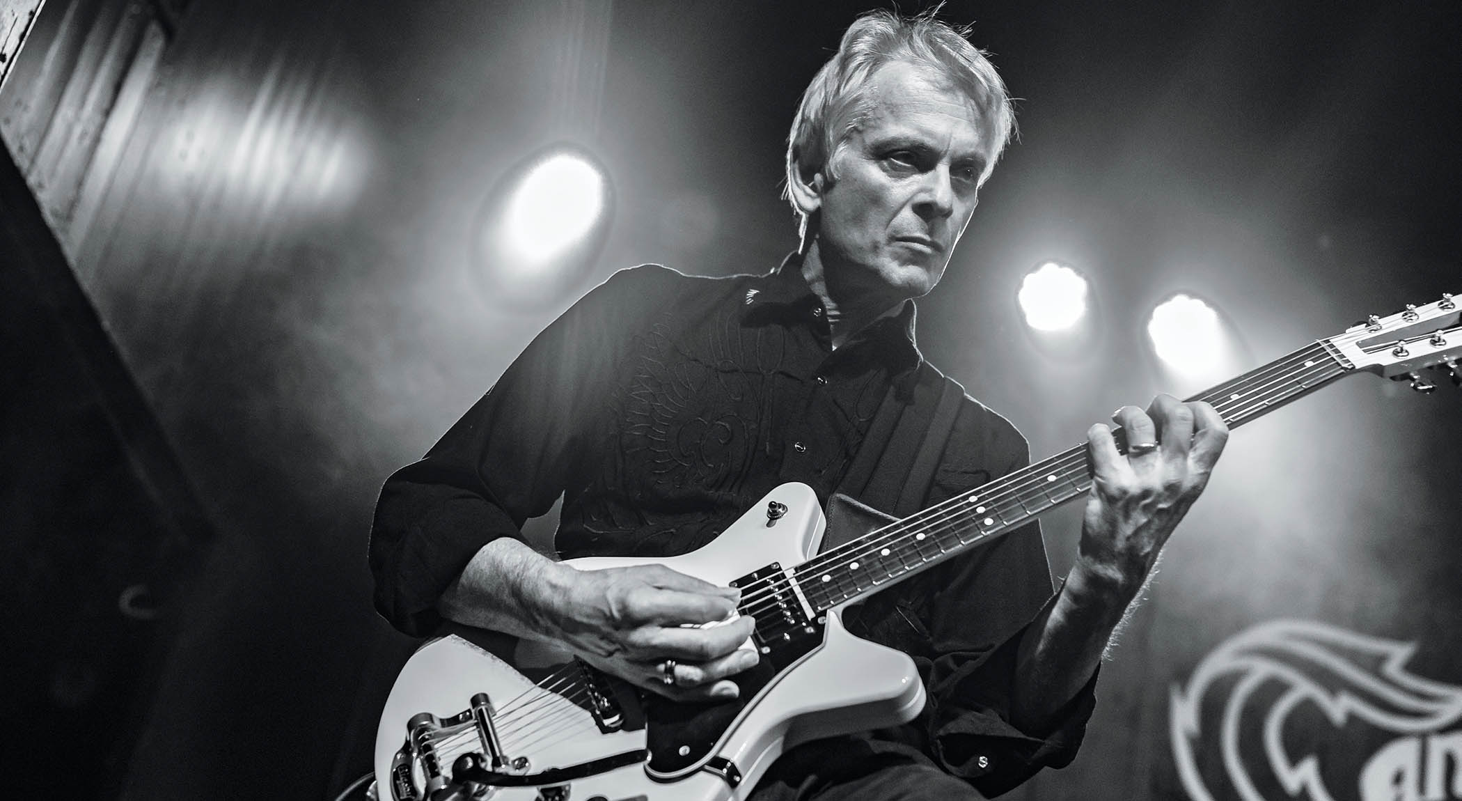 Duane Denison of The Jesus Lizard plays a chord on his Travis Bean electric guitar, in this black-and-white live shot from the audience's POV.